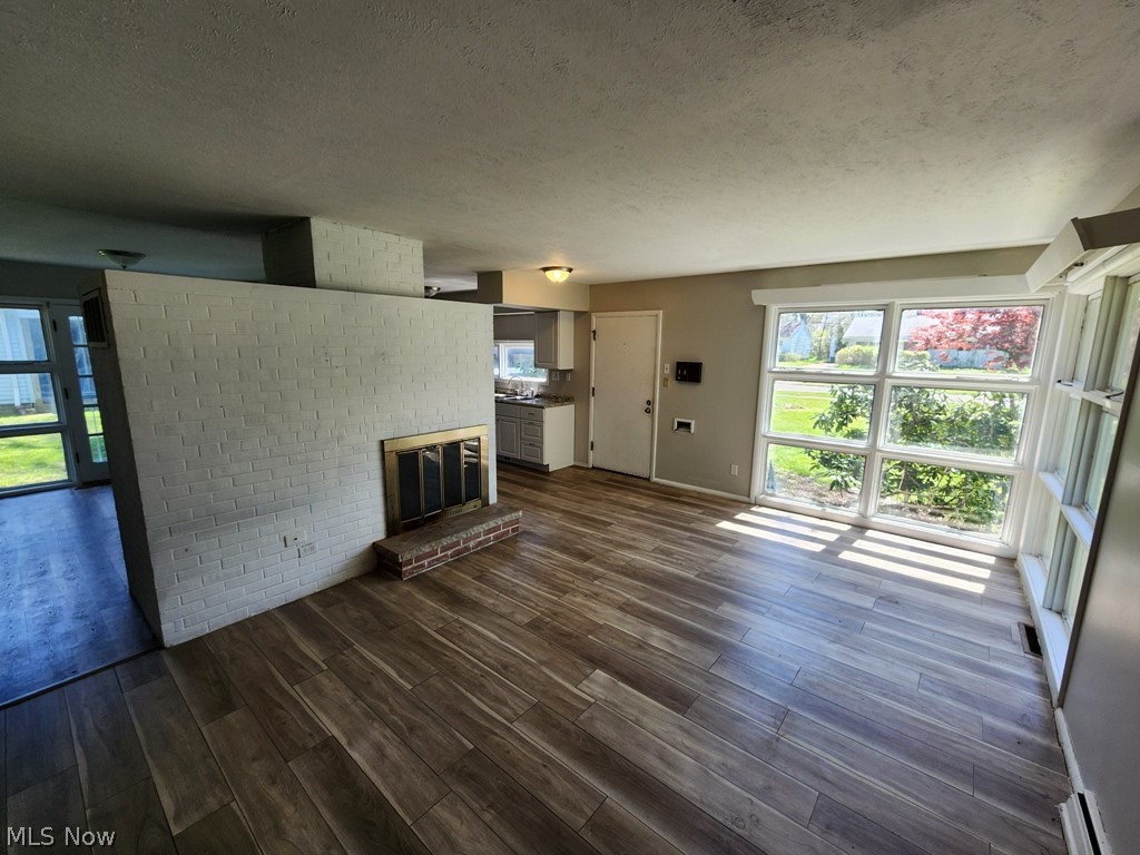 4061 Dartford Road Cleveland, OH 44121 - Photo 4 of 24 Unfurnished living room with a textured ceiling, brick wall, a brick fireplace, and dark wood-type flooring