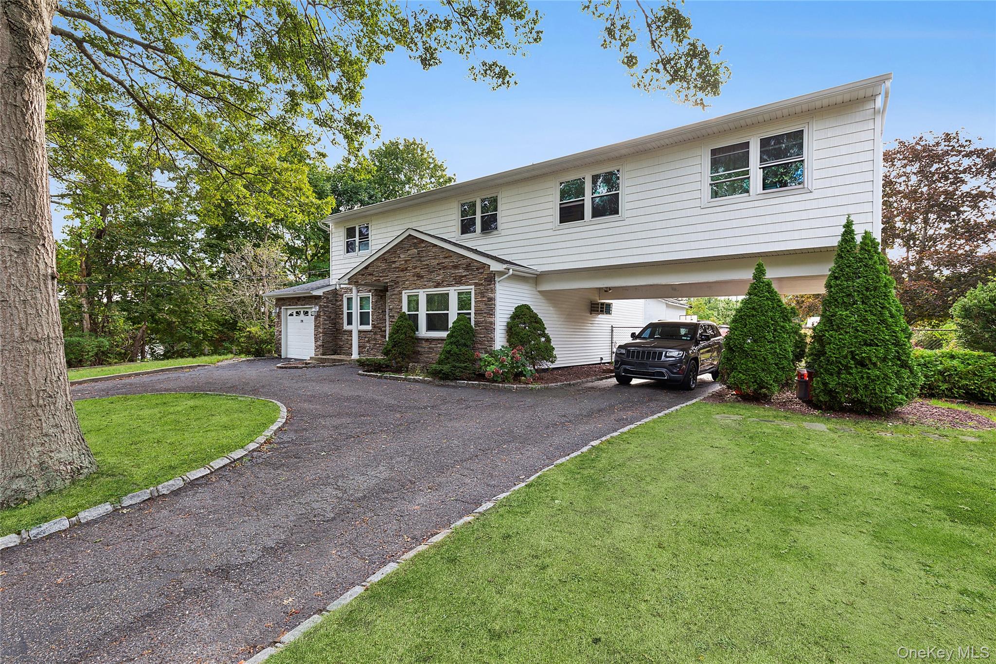 View of front of property with asphalt driveway, a front yard, a garage, and stone siding