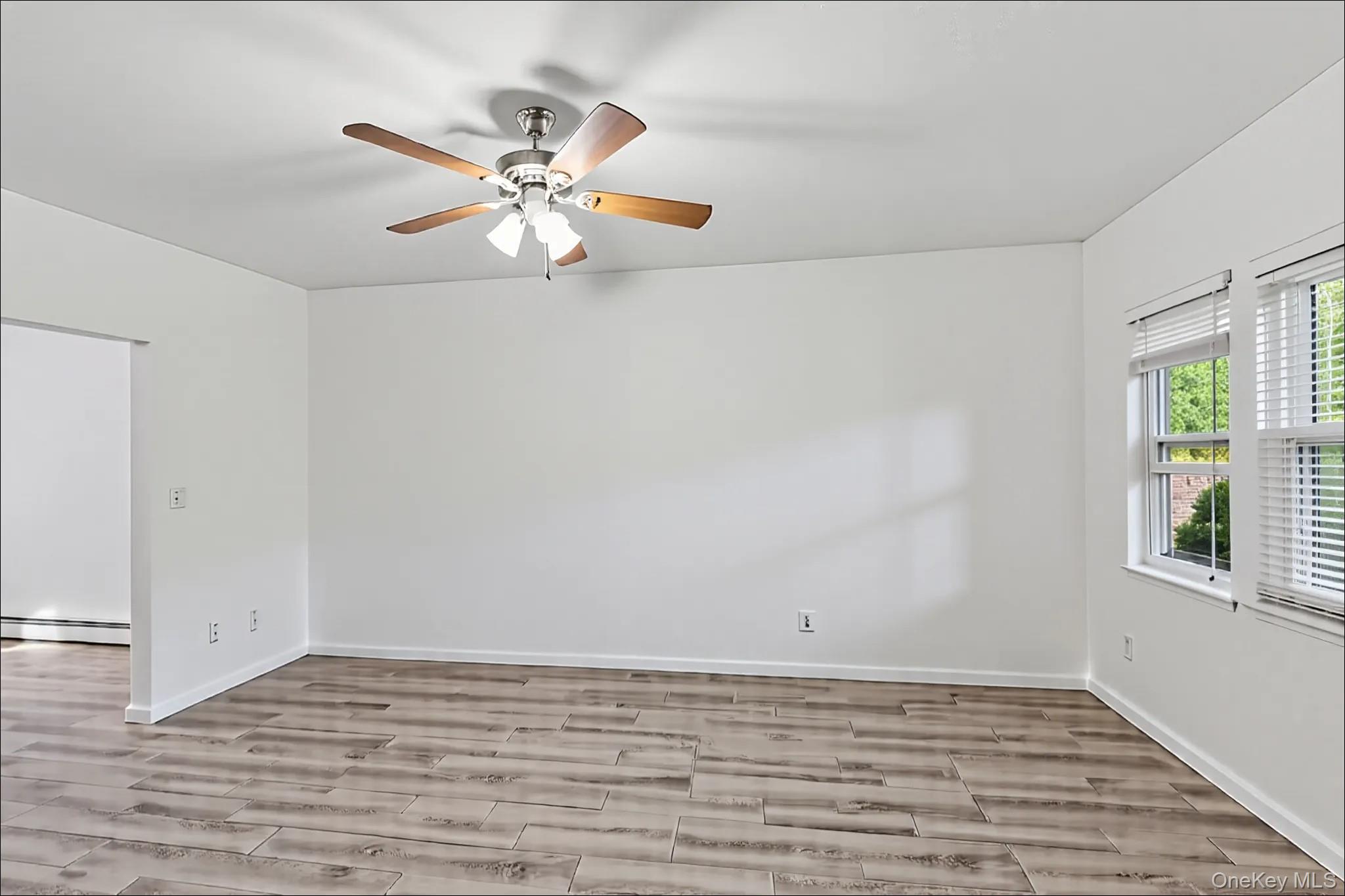 370 Blue Point Road Farmingville, NY 11738 - Photo 3 of 19 Empty room featuring wood finish floors, a baseboard heating unit, and ceiling fan