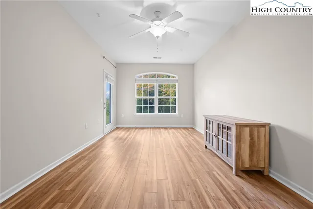 an empty room with wooden floor chandelier fan and windows