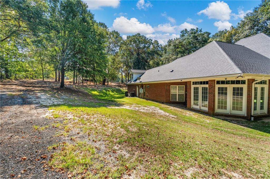 642 Nuckols Road Seale, AL 36875 - Photo 44 of 48 Brick exterior, multiple sets of French doors, asphalt shingle roof, mature trees, and a sloping grassy area