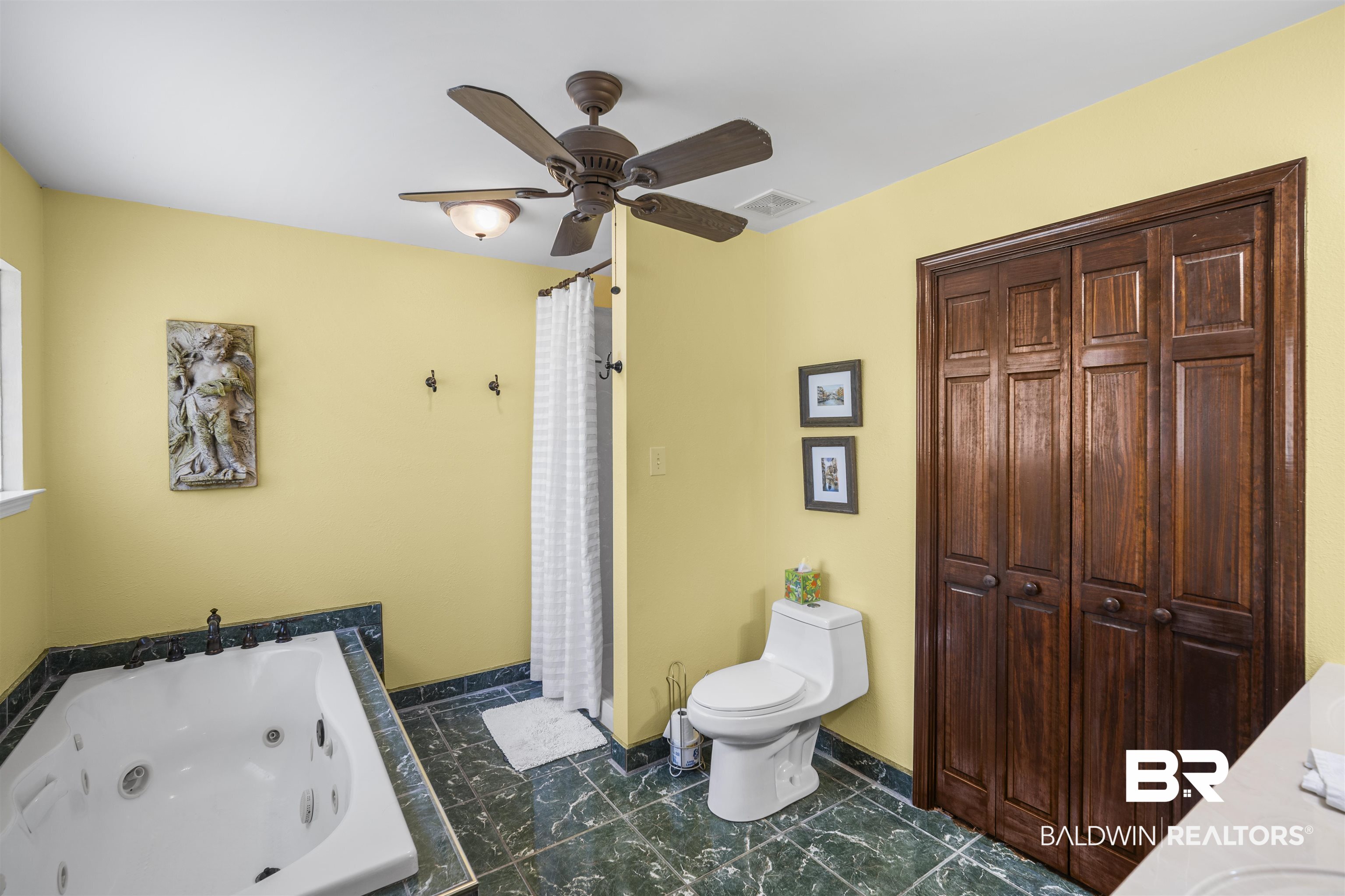 1615 5th Street Daphne, AL 36526 - Photo 17 of 28 Bathroom featuring a jetted soaking tub with dark stone surround, dark wood-finish bi-fold doors, a ceiling fan with integrated lighting, and dark patterned floor tiling