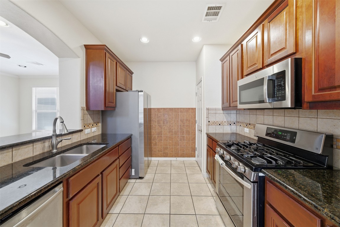 14100 Avery Ranch Boulevard, Unit 1502 Austin, TX 78717 - Photo 11 of 39 Kitchen featuring stainless steel appliances, dark stone counters, light tile patterned floors, brown cabinetry, and wainscoting