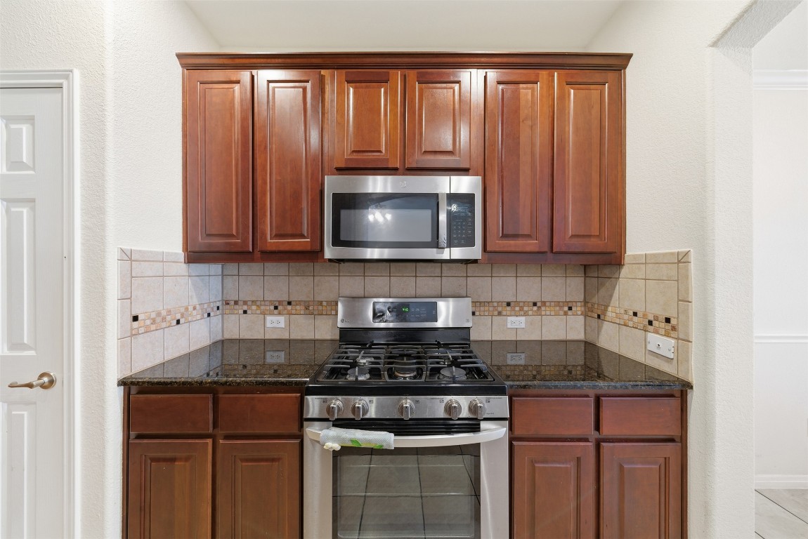 14100 Avery Ranch Boulevard, Unit 1502 Austin, TX 78717 - Photo 12 of 39 Kitchen featuring appliances with stainless steel finishes, dark stone countertops, decorative backsplash, and brown cabinetry