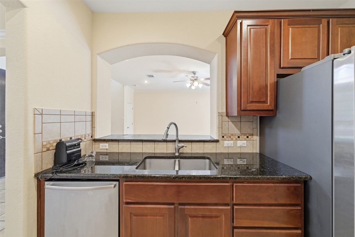 14100 Avery Ranch Boulevard, Unit 1502 Austin, TX 78717 - Photo 13 of 39 Kitchen featuring stainless steel appliances, brown cabinetry, dark stone counters, backsplash, and a ceiling fan
