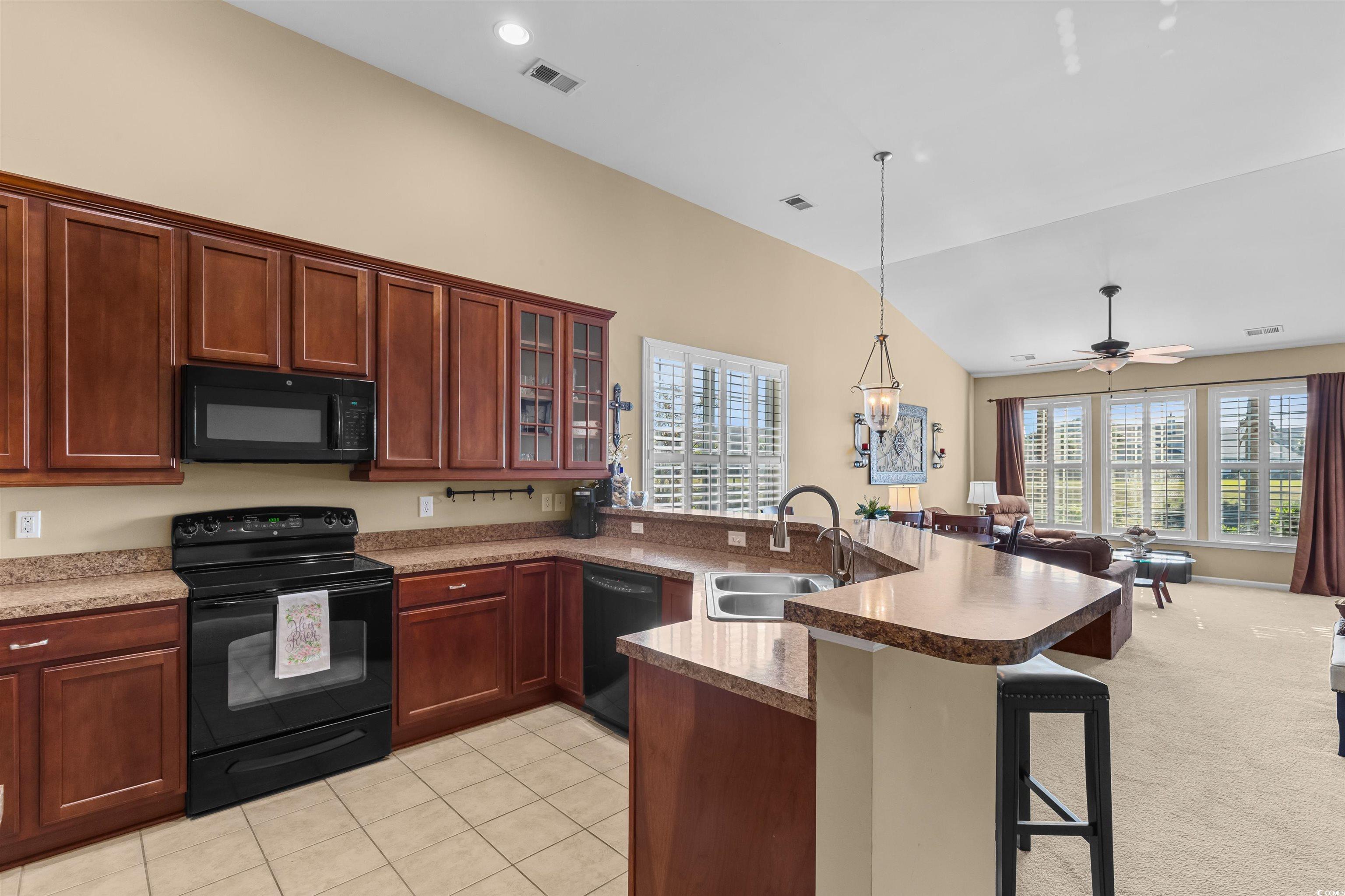 3233 Volterra Way, Unit 3233 Myrtle Beach, SC 29579 - Photo 9 of 40 Kitchen with black appliances, a breakfast bar, glass insert cabinets, a peninsula, and vaulted ceiling