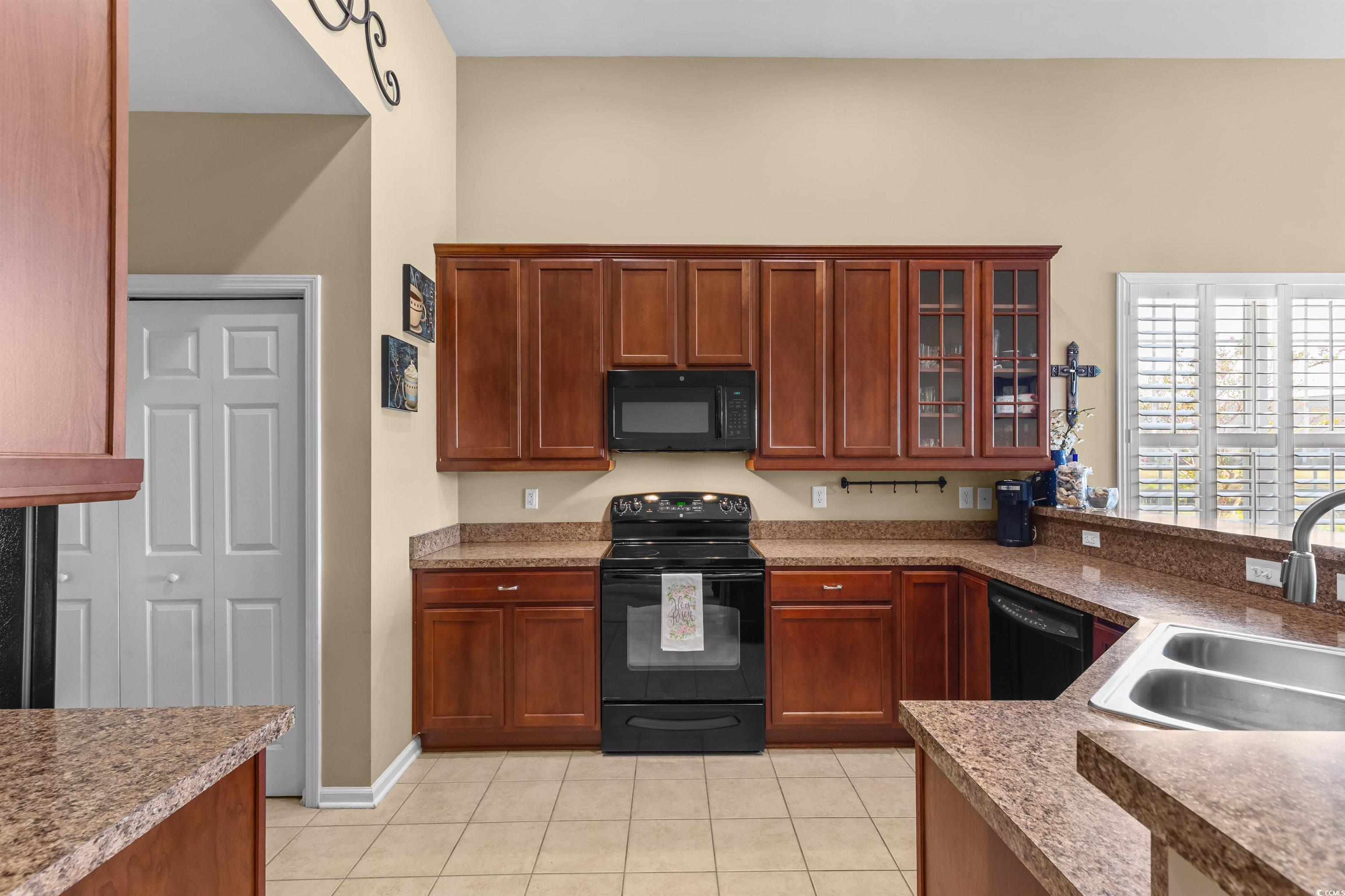 3233 Volterra Way, Unit 3233 Myrtle Beach, SC 29579 - Photo 10 of 40 Kitchen featuring black appliances, light tile patterned flooring, glass insert cabinets, and brown cabinets