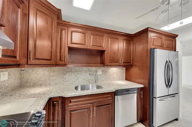 a kitchen with stainless steel appliances granite countertop a refrigerator a stove and a sink with wooden cabinets