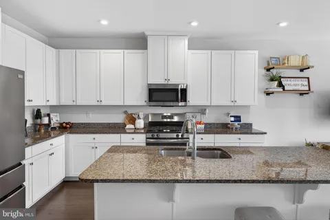 a kitchen with kitchen island granite countertop a sink a stove a microwave and wooden cabinets