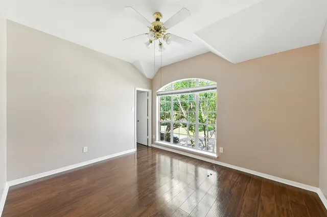 an empty room with wooden floor chandelier fan and windows