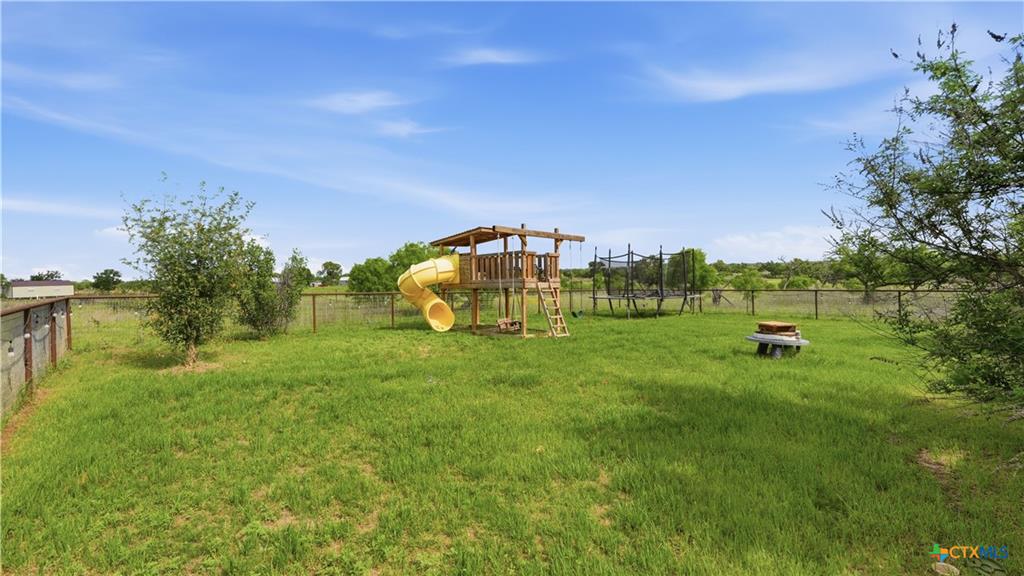 127 Offer Llano, TX 78643 - Photo 37 of 40 Expansive fenced backyard featuring a wooden play structure with yellow slide, mature trees, and a fire pit