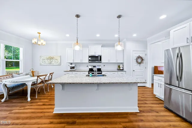 a large kitchen with granite countertop a stove a sink a refrigerator and a dining table with wooden floor