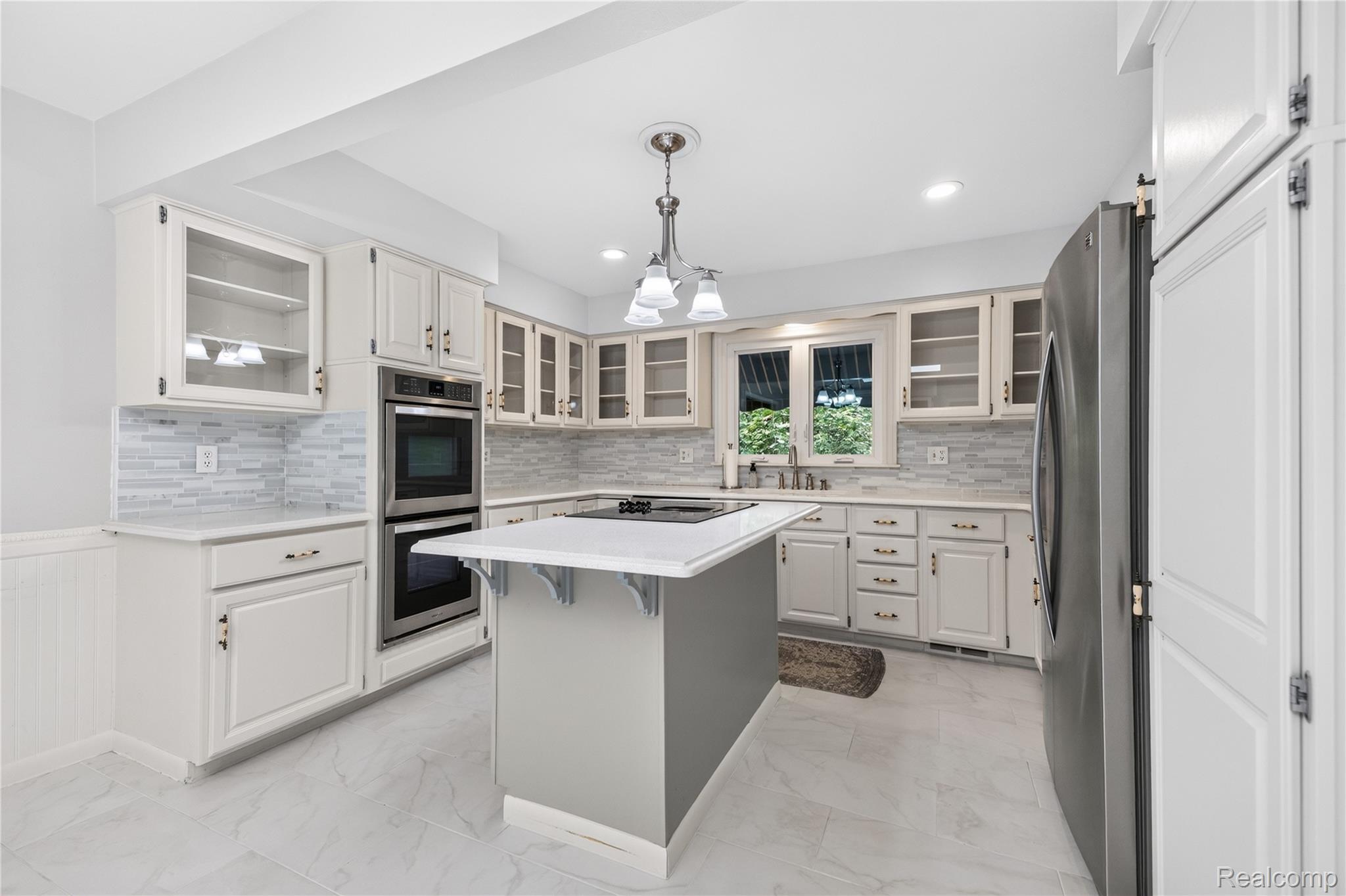 25645 Meridian Road Grosse Ile, MI 48138 - Photo 8 of 46 Kitchen featuring white cabinetry, a center island with a cooktop, double wall ovens, a stainless steel refrigerator, and tiled flooring