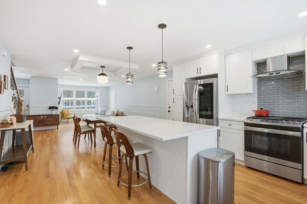 27 Pine Street, Unit 27 Dedham, MA 02026 - Photo 7 of 35 a kitchen with stainless steel appliances kitchen island granite countertop a stove a refrigerator a oven a dining table and chairs with wooden floor