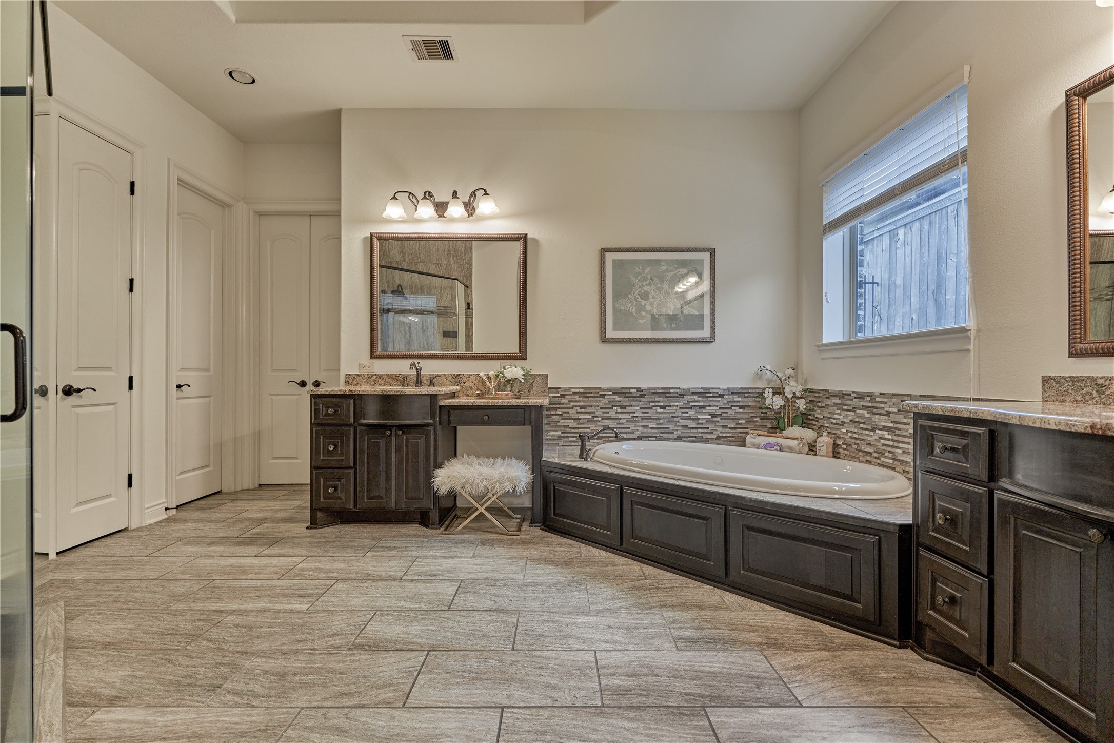 108 Evergreen Oak Drive Conroe, TX 77384 - Photo 23 of 45 This spacious bathroom features elegant tile flooring, a large soaking tub with stylish tile backsplash, dual sink vanities with dark wood cabinets, and ample natural light from a sizable window.