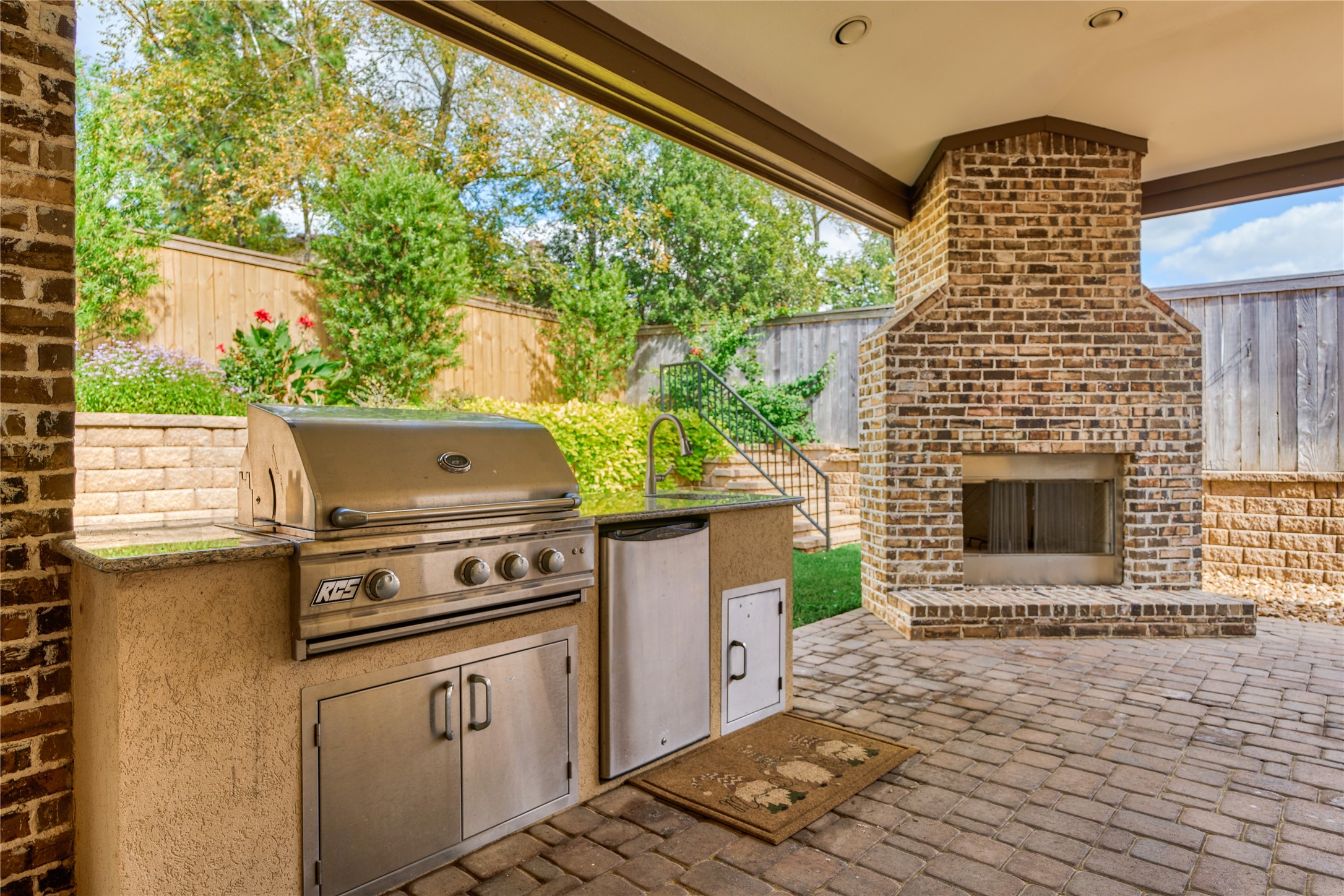 108 Evergreen Oak Drive Conroe, TX 77384 - Photo 41 of 45 This outdoor living space features a built-in stainless steel grill and a brick fireplace, perfect for entertaining. It includes a paved patio with lush landscaping and privacy fencing, creating a cozy and inviting atmosphere.