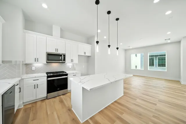 a large kitchen with stainless steel appliances kitchen island granite countertop a stove a sink a refrigerator and white cabinets with wooden floor