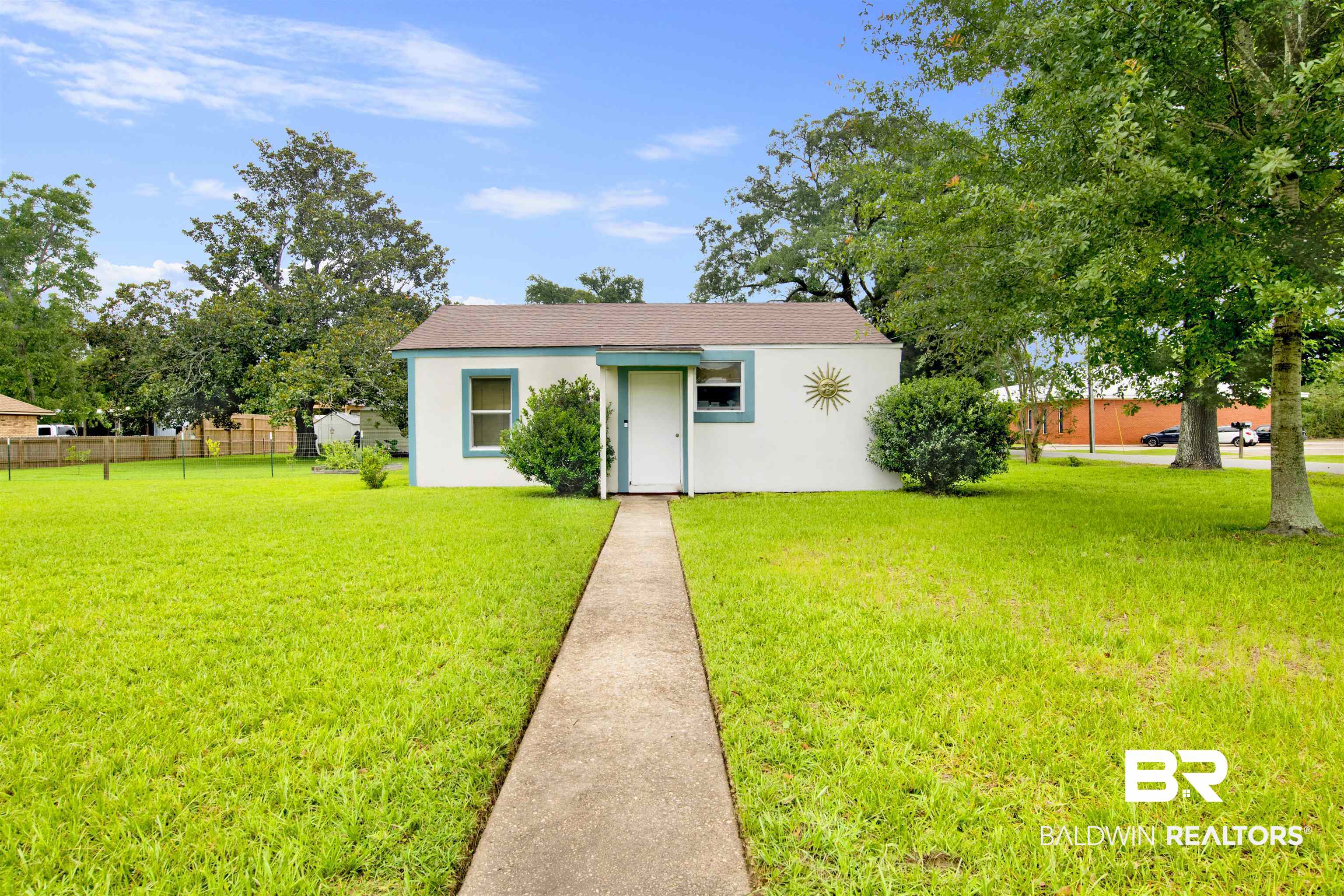 1100 North Pine Street Foley, AL 36535 - Photo 1 of 30 Single-story residence featuring a white exterior with teal trim accents, a concrete pathway, a shingled roof, a mature tree, and a spacious front lawn