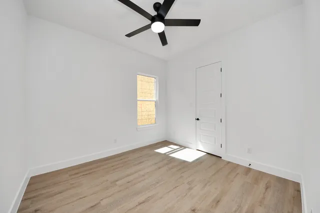 an empty room with wooden floor ceiling fan and windows