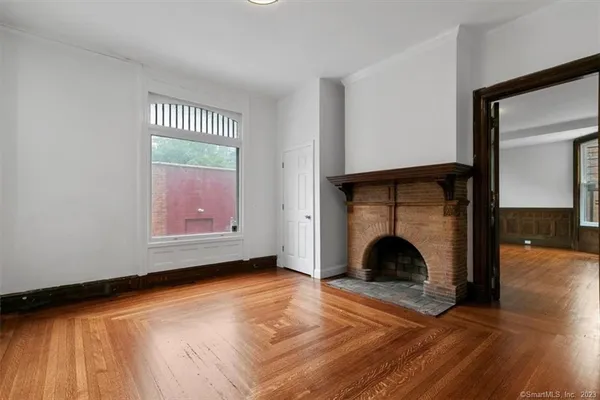 a view of an empty room with wooden floor fireplace and a window