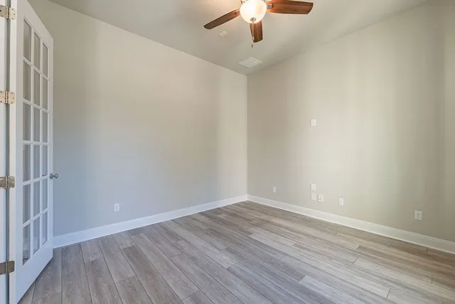 a view of an empty room with wooden floor and a kitchen
