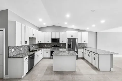 a large white kitchen with stainless steel appliances granite countertop a stove and a sink