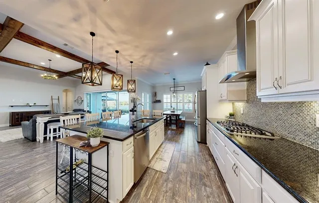 a large kitchen with stainless steel appliances kitchen island granite countertop a sink dishwasher a stove and a dining table with wooden floor