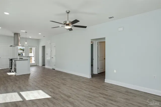 a view of an empty room with wooden floor and a kitchen