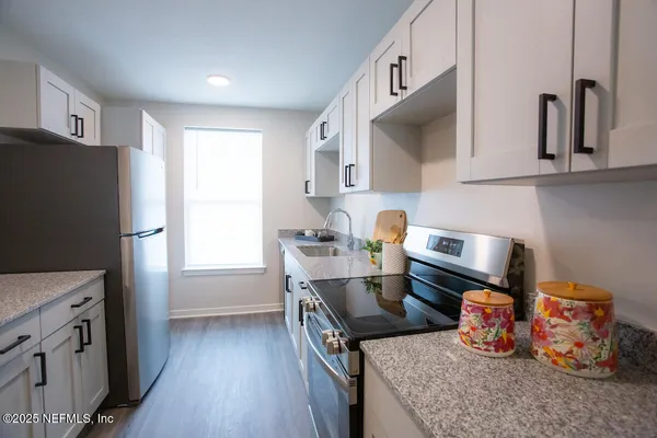 a kitchen with stainless steel appliances granite countertop a refrigerator a sink dishwasher a stove and a dining table with wooden floor