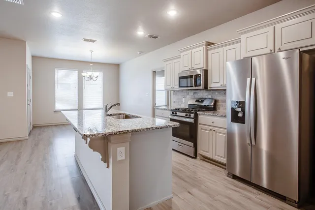 a kitchen with stainless steel appliances granite countertop a refrigerator a stove a sink dishwasher and a refrigerator with wooden floor