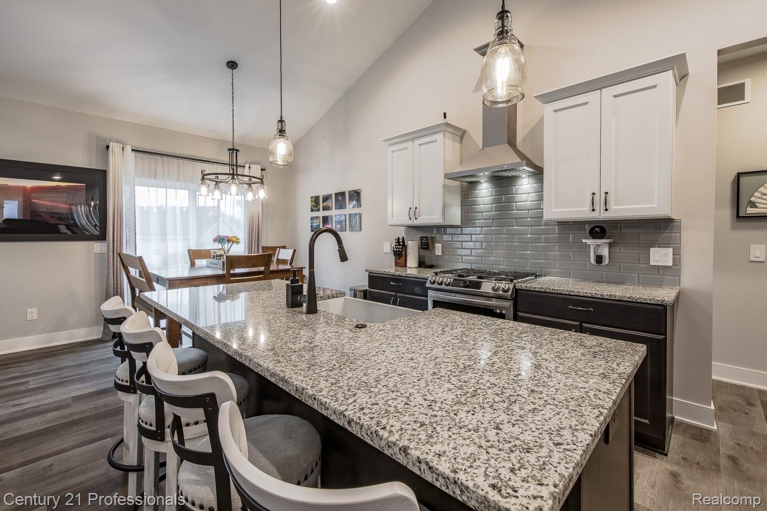 4914 TORATOLA Lane Howell, MI 48843 - Photo 17 of 39 Dual tone kitchen with vaulted ceiling, dark wood finished floors, stainless steel gas range oven, light stone counters, and pendant lighting