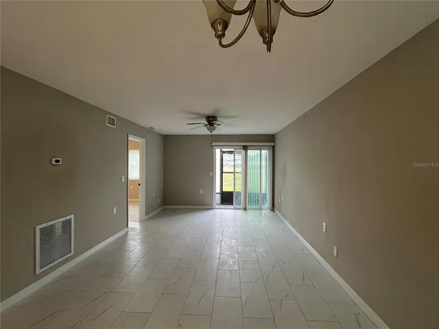 a view of an empty room with window and chandelier fan