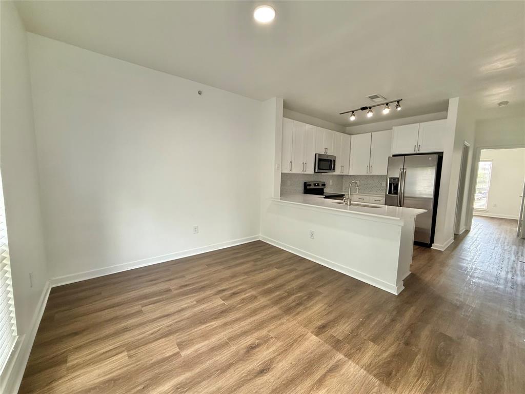 Kitchen featuring stainless steel appliances, a peninsula, tasteful backsplash, white cabinets, and light countertops