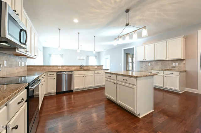 a kitchen with stainless steel appliances granite countertop a stove top oven a sink a refrigerator and white cabinets with wooden floor