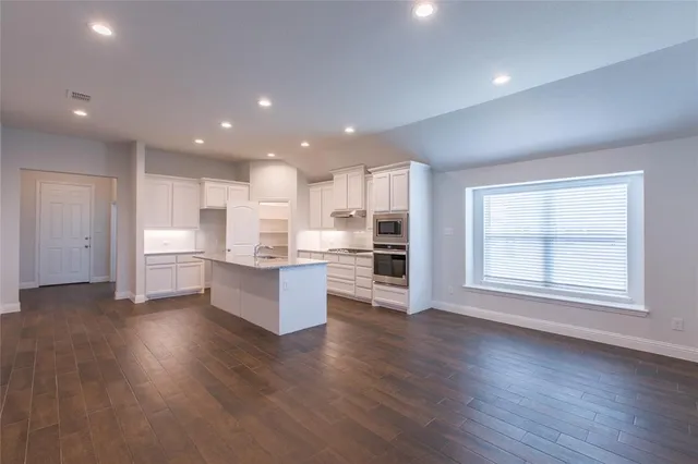 a large kitchen with stainless steel appliances granite countertop a large counter top a wooden floors and a large window