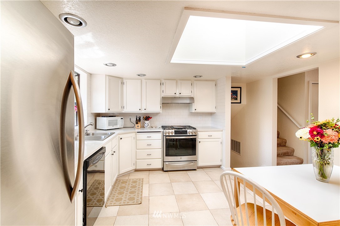 7902 211th Place Southwest Edmonds, WA 98026 - Photo 28 of 33 a kitchen with stainless steel appliances kitchen island granite countertop a refrigerator a sink dishwasher and white cabinets with wooden floor