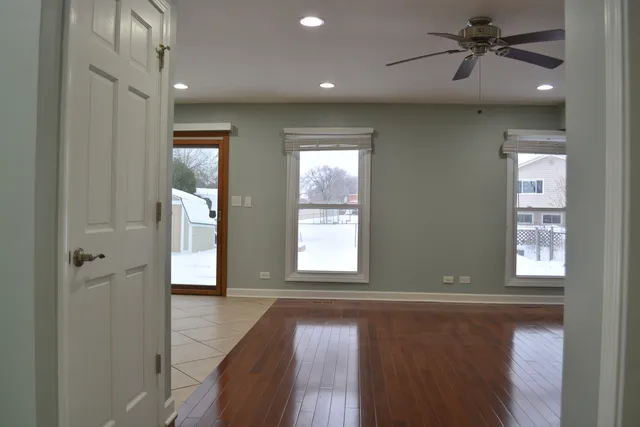an empty room with wooden floor ceiling fan and windows