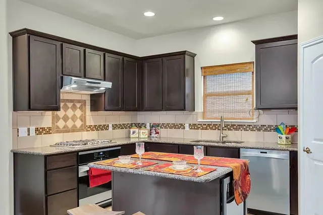 a utility room with stainless steel appliances kitchen island granite countertop a sink and a stove