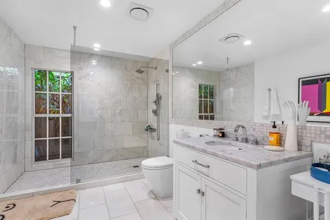 a bathroom with a granite countertop sink a toilet a mirror and shower