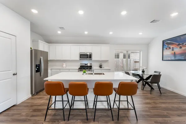 a dining hall with stainless steel appliances granite countertop a stove a sink a dining table and chairs with wooden floor