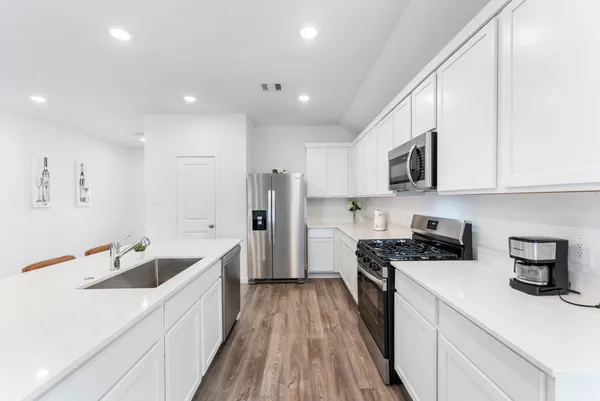 a kitchen with stainless steel appliances kitchen island granite countertop a dining table chairs refrigerator and wooden cabinets