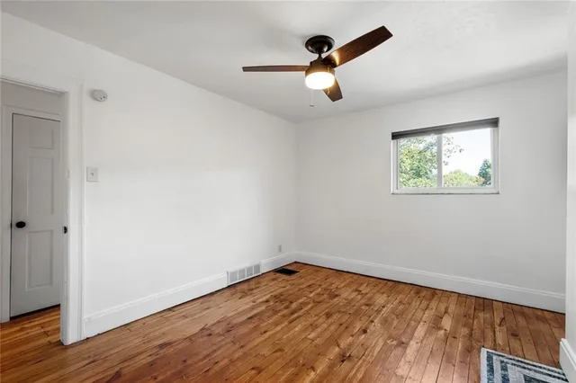 an empty room with wooden floor chandelier fan and windows