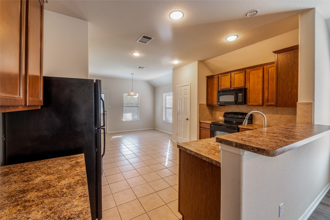 200 Falcon Lane Leander, TX 78641 - Photo 6 of 20 Kitchen featuring brown cabinetry, black appliances, light tile patterned floors, backsplash, and vaulted ceiling