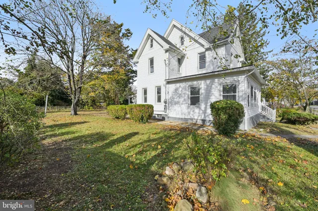 a view of a white house next to a yard with big trees