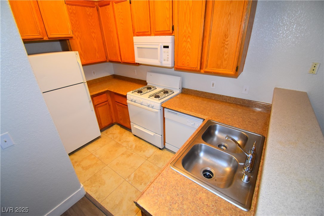 4730 East Craig Road, Unit 2094 Las Vegas, NV 89115 - Photo 2 of 12 Kitchen with white appliances, light countertops, a textured wall, brown cabinets, and light tile patterned floors