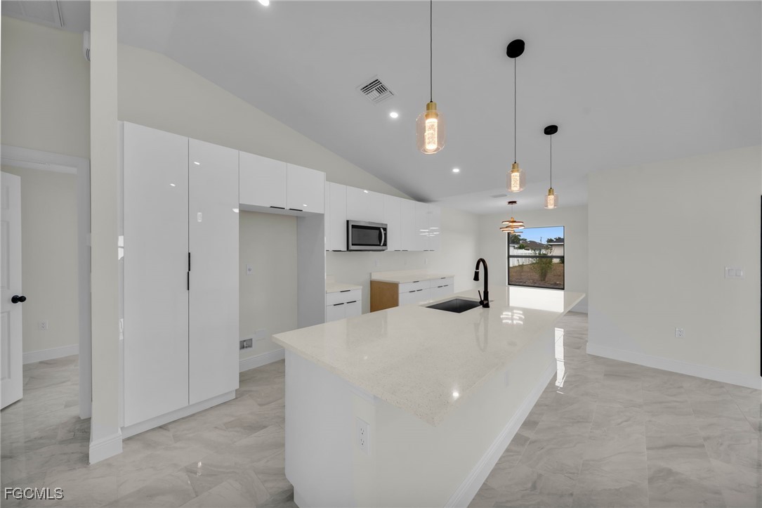 4106 35th Street Southwest Lehigh Acres, FL 33976 - Photo 10 of 38 a large white kitchen with kitchen island a refrigerator a sink dishwasher with a dining table and chairs