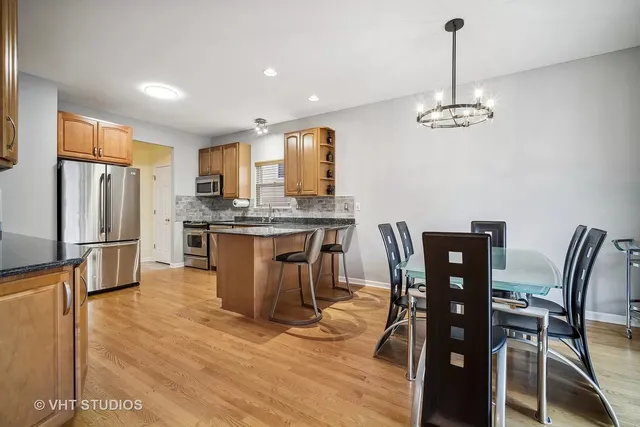 a kitchen with stainless steel appliances kitchen island granite countertop a dining table chairs refrigerator and sink