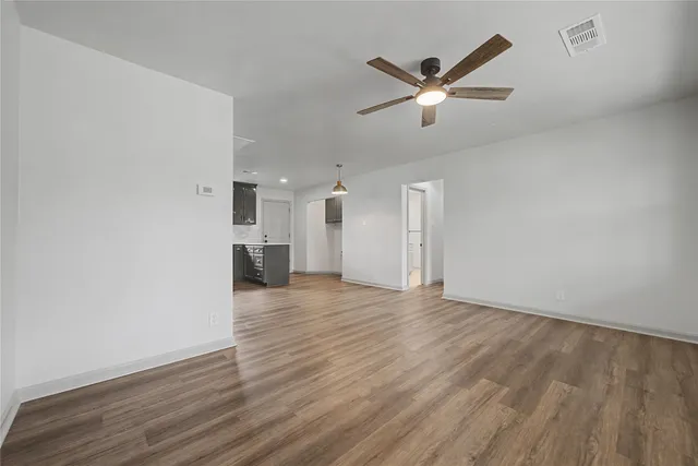 a view of an empty room with wooden floor and a ceiling fan