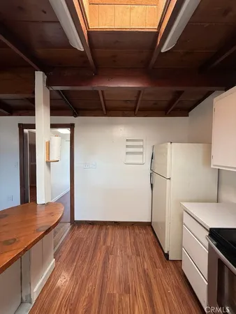 a view of a refrigerator in kitchen and an empty room with wooden floor