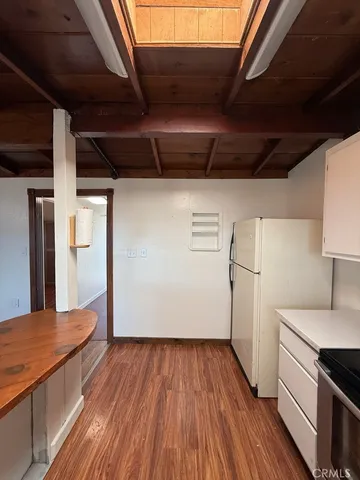 a view of a refrigerator in kitchen and an empty room with wooden floor